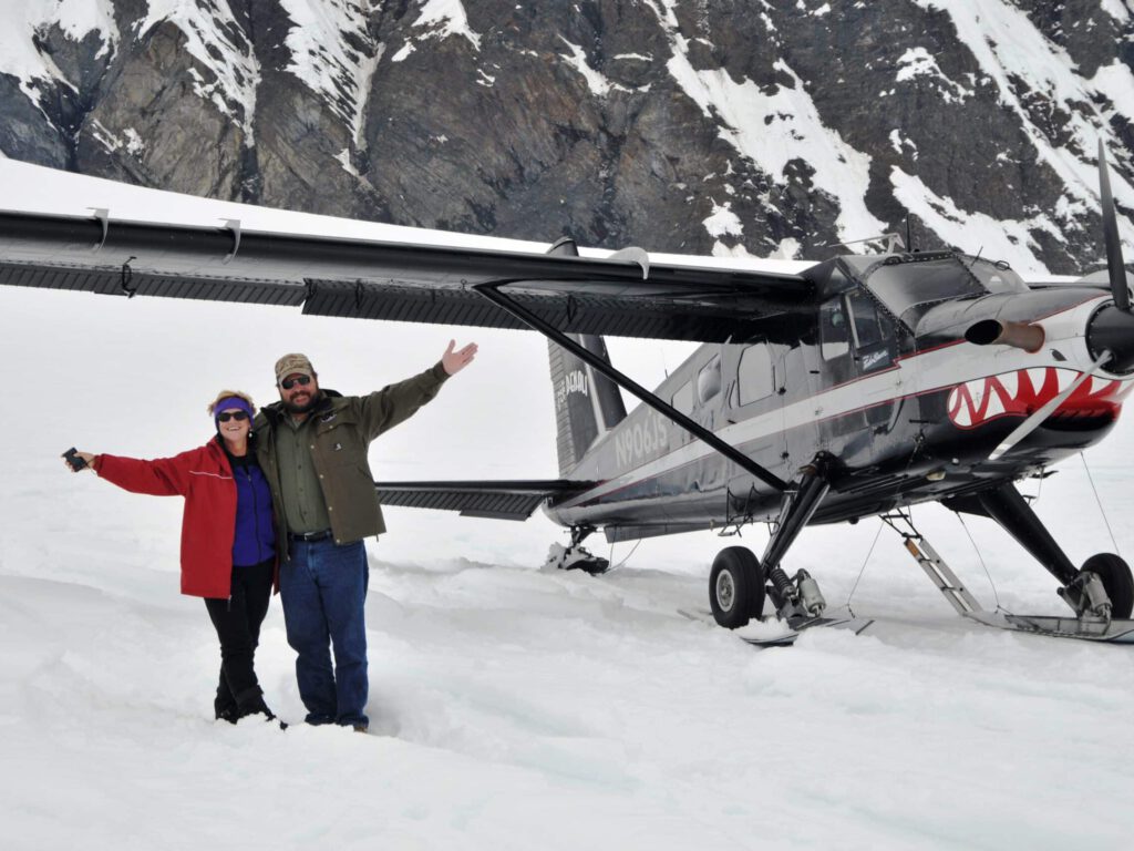 A couple poses by the plane as they stand on a glacier.
