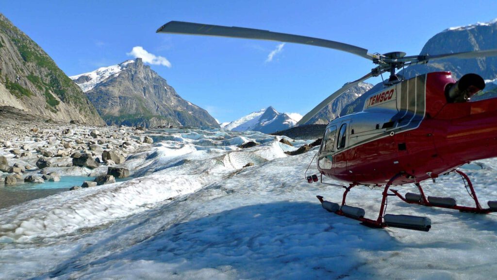 A helicopter charter lands on the ice above a glacier pool.