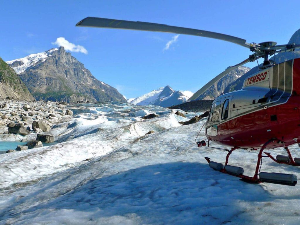 A helicopter charter lands on the ice above a glacier pool.