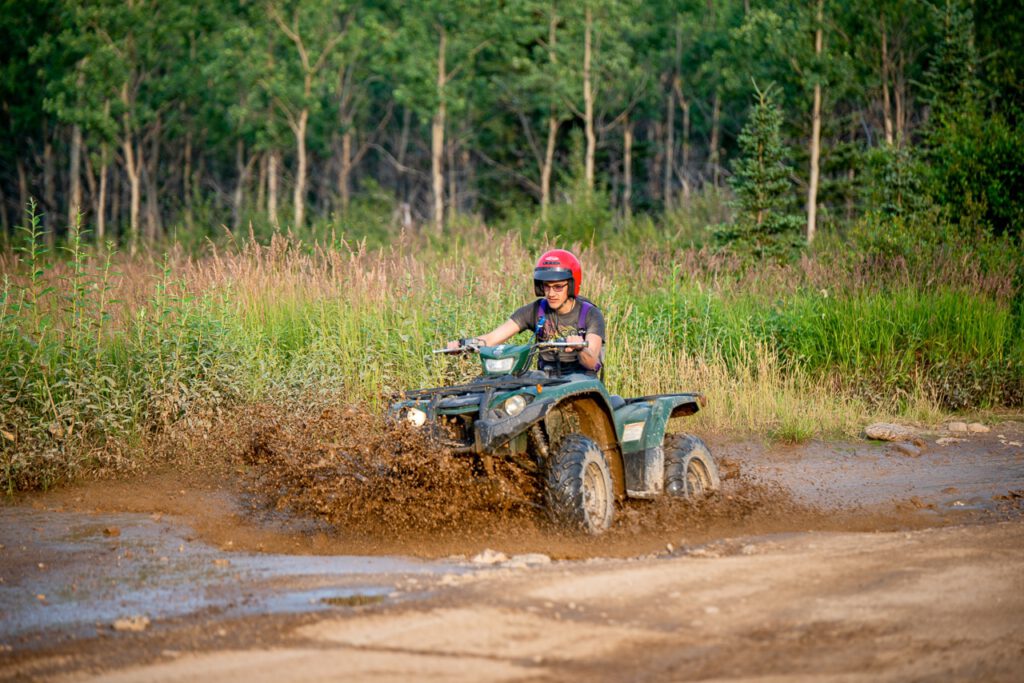 A single rider ATV splashes through a muddy section of the trail.