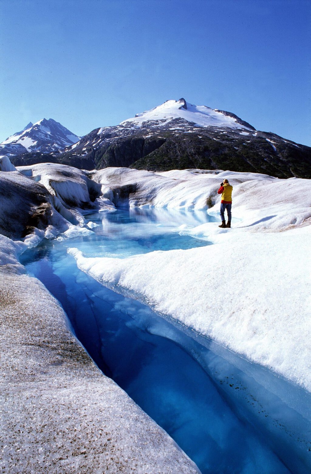A woman photographs a blue pool on a glacier.