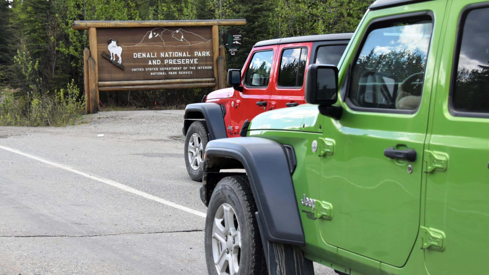 Two Jeeps are parked near the welcome sign near the entrance of Denali National Park.